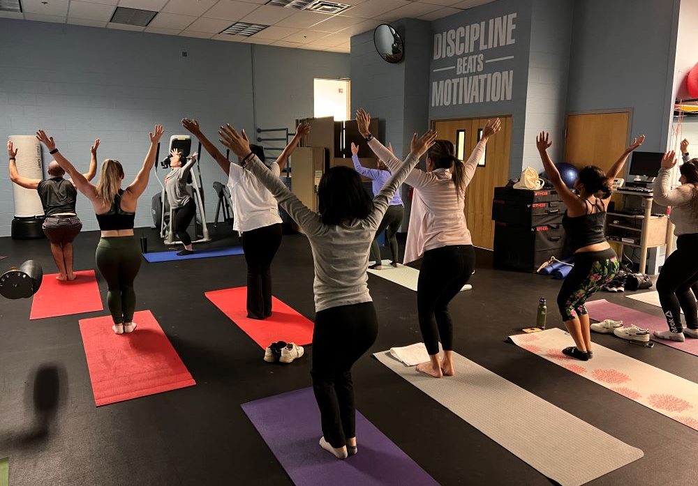 People stand on yoga mats with their hands making a V above their heads in the fitness center