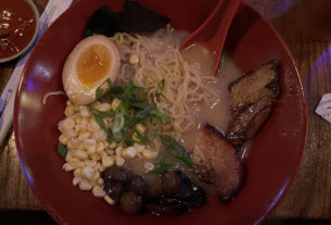 A red bowl of ramen with meat, eggs, vegetables, and noodles.