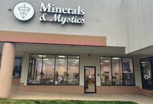 The cement building with large windows that at the front enterance of Minerals & Mystics