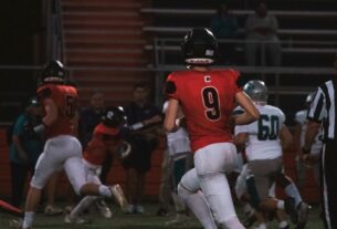 A group of football players in full outfit running across a field at night.