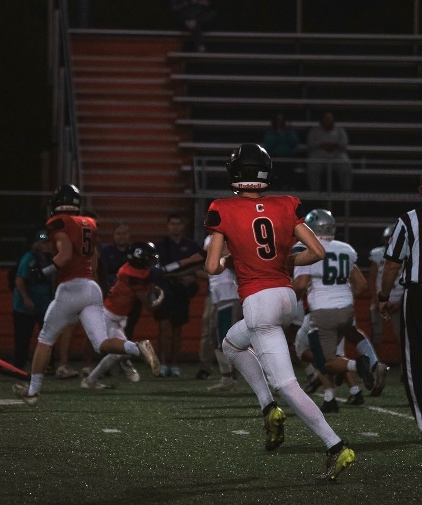 A group of football players in full outfit running across a field at night.