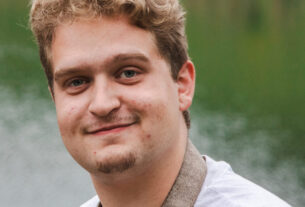 A man with blonde hair and goatee standing next to a pond.