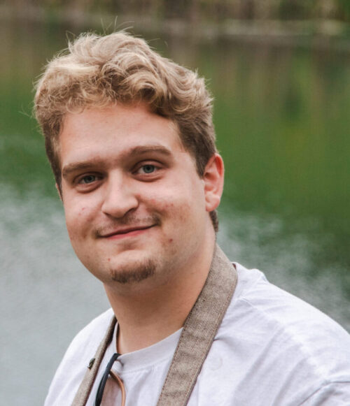 A man with blonde hair and goatee standing next to a pond.