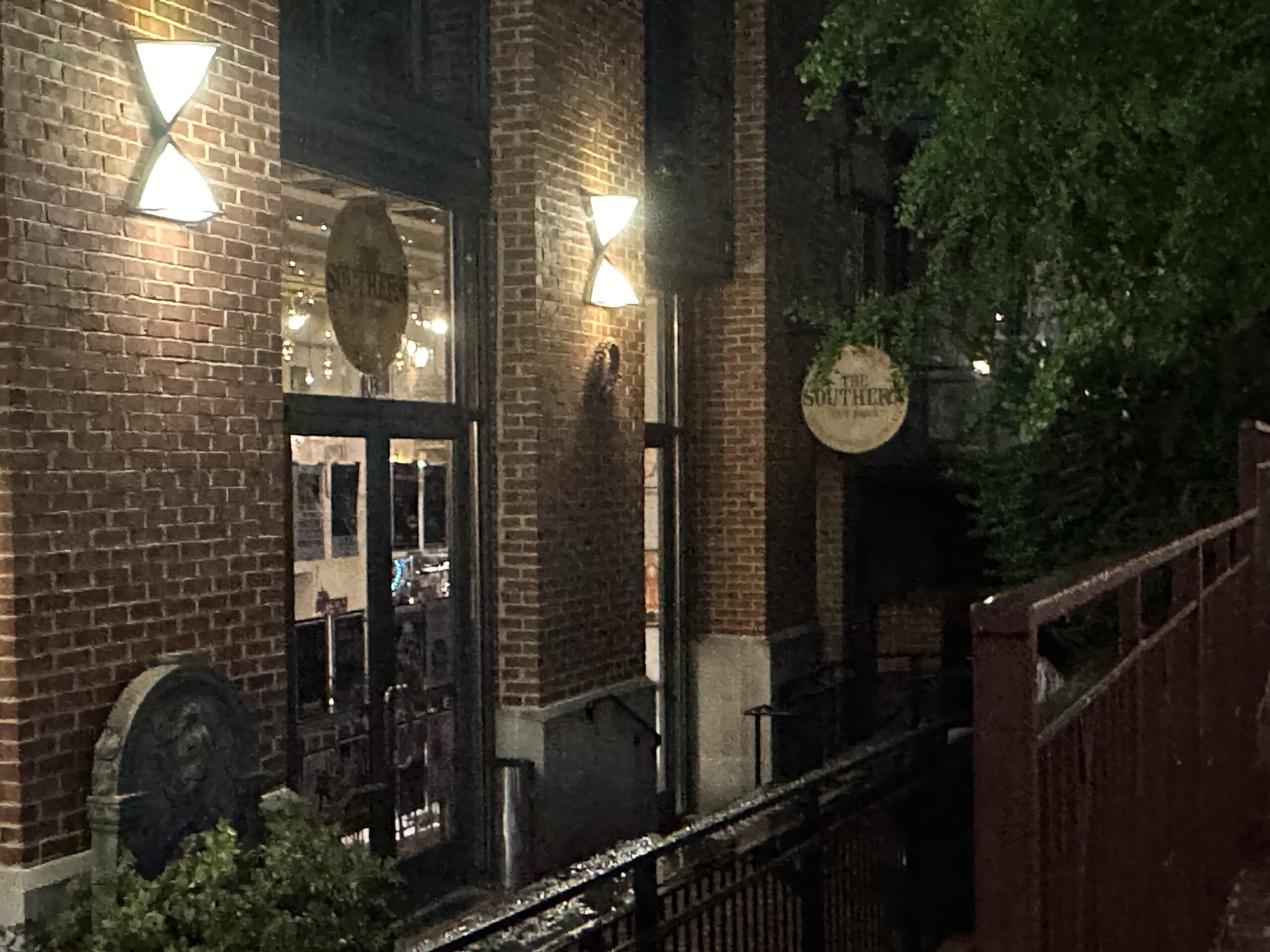 A night image of glass doors on the side of brick building with circular signs for The Southern.