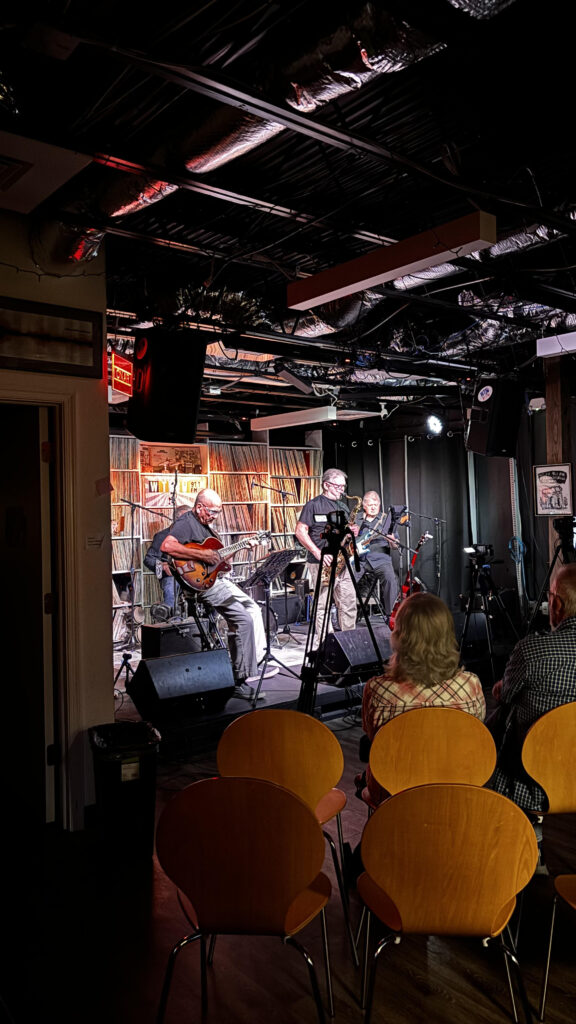 An audience watches as 5 jazz musicians play in a studio.