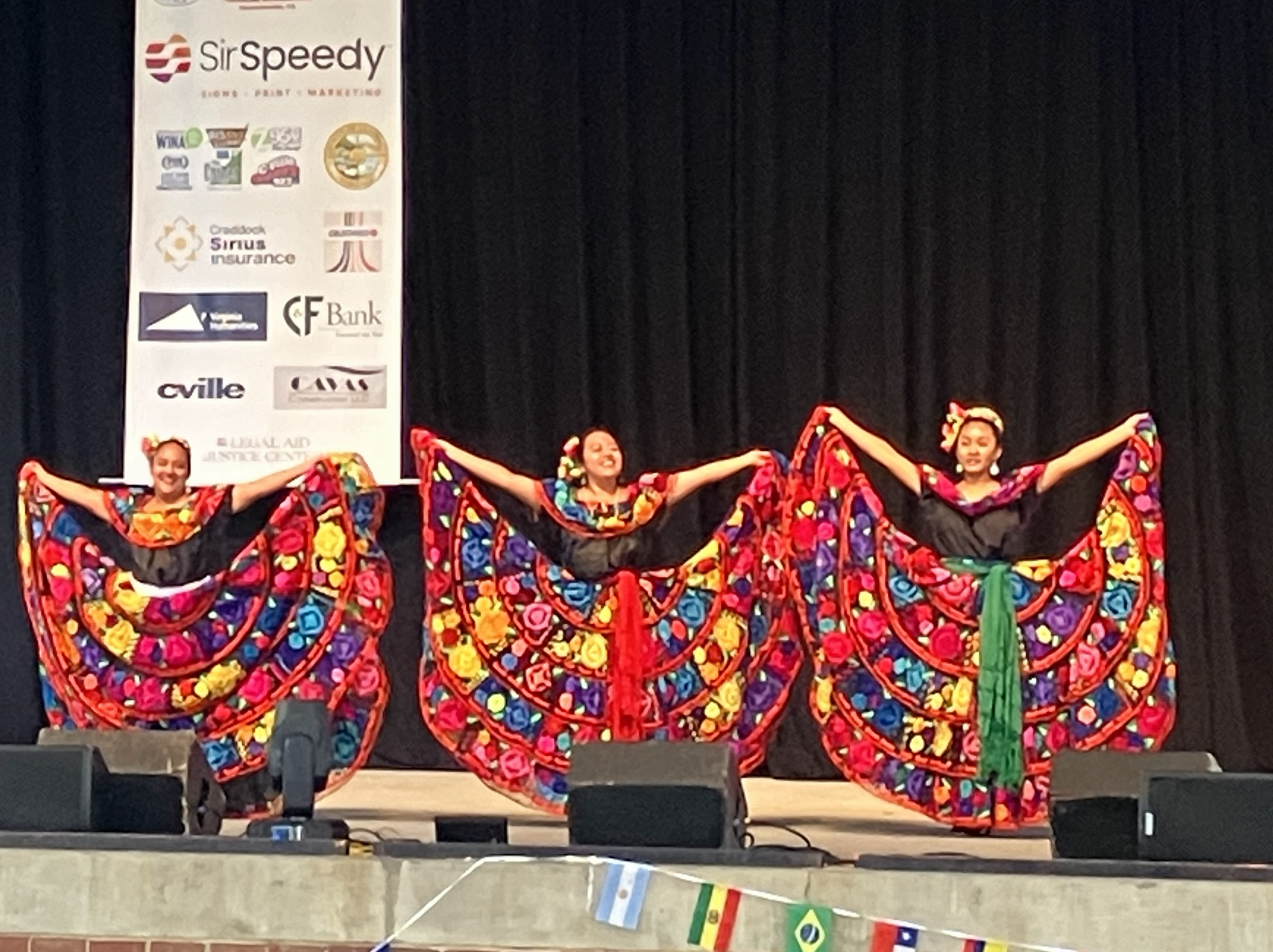 Three dancers stand on a stage wearing ornate dresses.