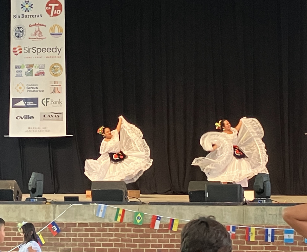 Two dancers wearing white ornate dresses twirl their skirts on a stage.