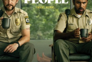 Joseph Gorden-Levitt and Himesh Patel both wearing police uniforms sit facing a pile of money on a bed. Behind them two feet of a body show on the floor. It is the poster for the film