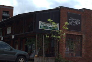 A brick building, known as the Downtown Design Center, sits across from train tracks.