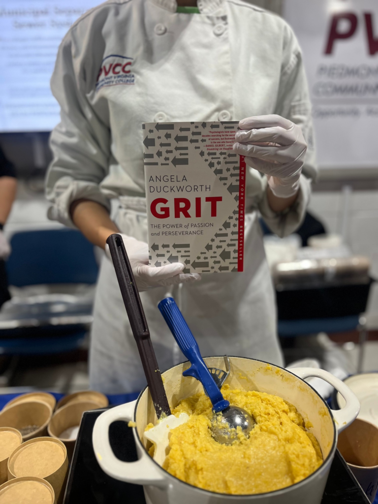 A Culinary Arts student holds a copy of Angela Duckworth's Grit above a table with a pot of grits.