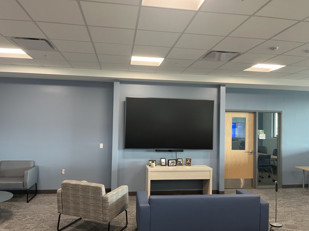 A leather couch and cloth armchair face a television screen.