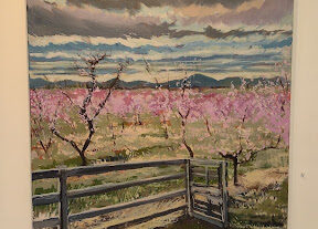 An oil painting of peach blossoms on canvas hangs on a wall.