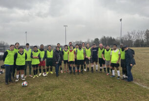 A group of soccer players wearing light green attire pose for a group photo on a grassy field.