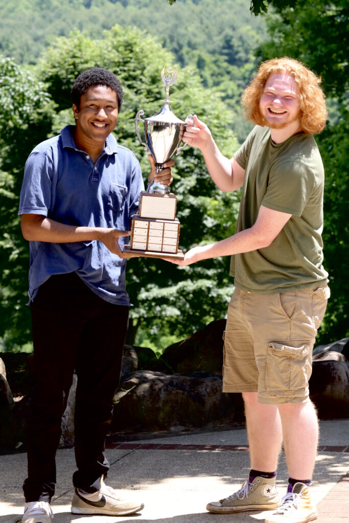 Two men hold up a large chrome soccer trophy.