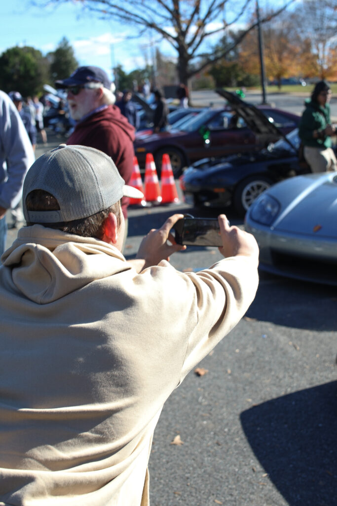 An attendant wearing a baseball cap leans in for a perfect shot of the grey Koenigsegg CCXR with his iPhone.