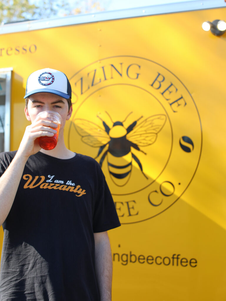 An attendant sips iced tea in front of the yellow Buzzing Bee Coffee food truck. Photography by Alex Warner