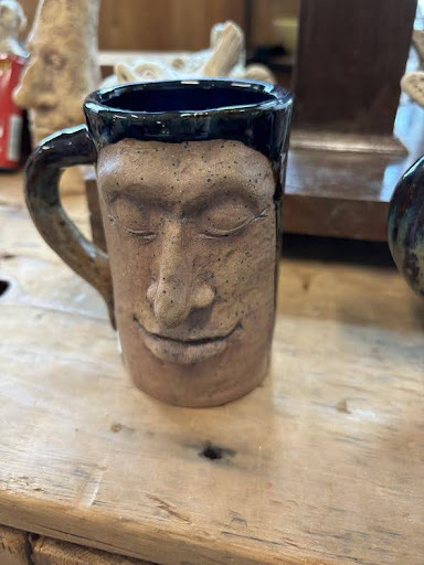 A clay mug carved with a face sitting on a wooden table