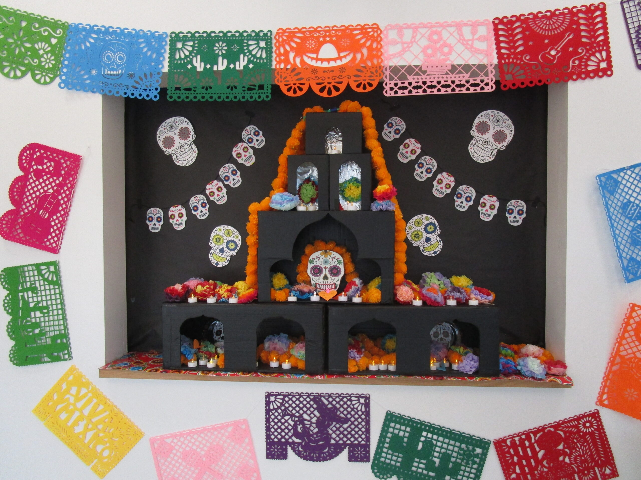 A decorative ofrenda with stencil cutouts made of paper surrounding it.