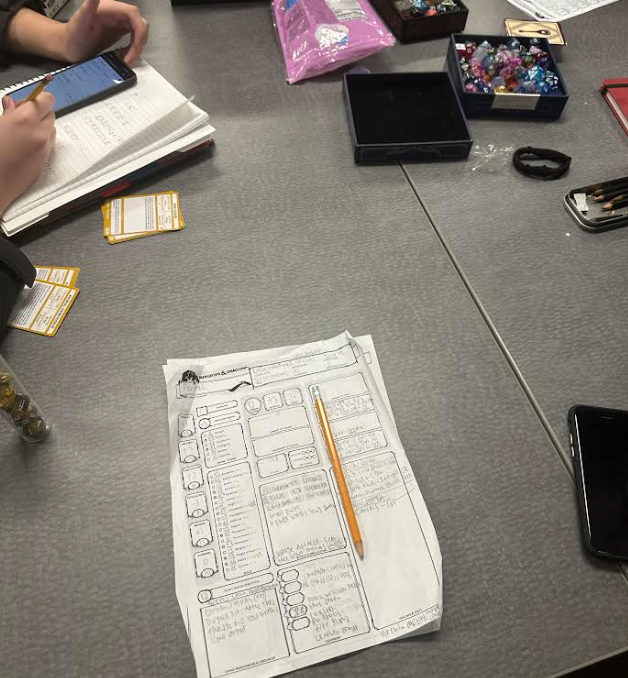 A tabletop with a box of dice, some paper, and a D&D character sheet.