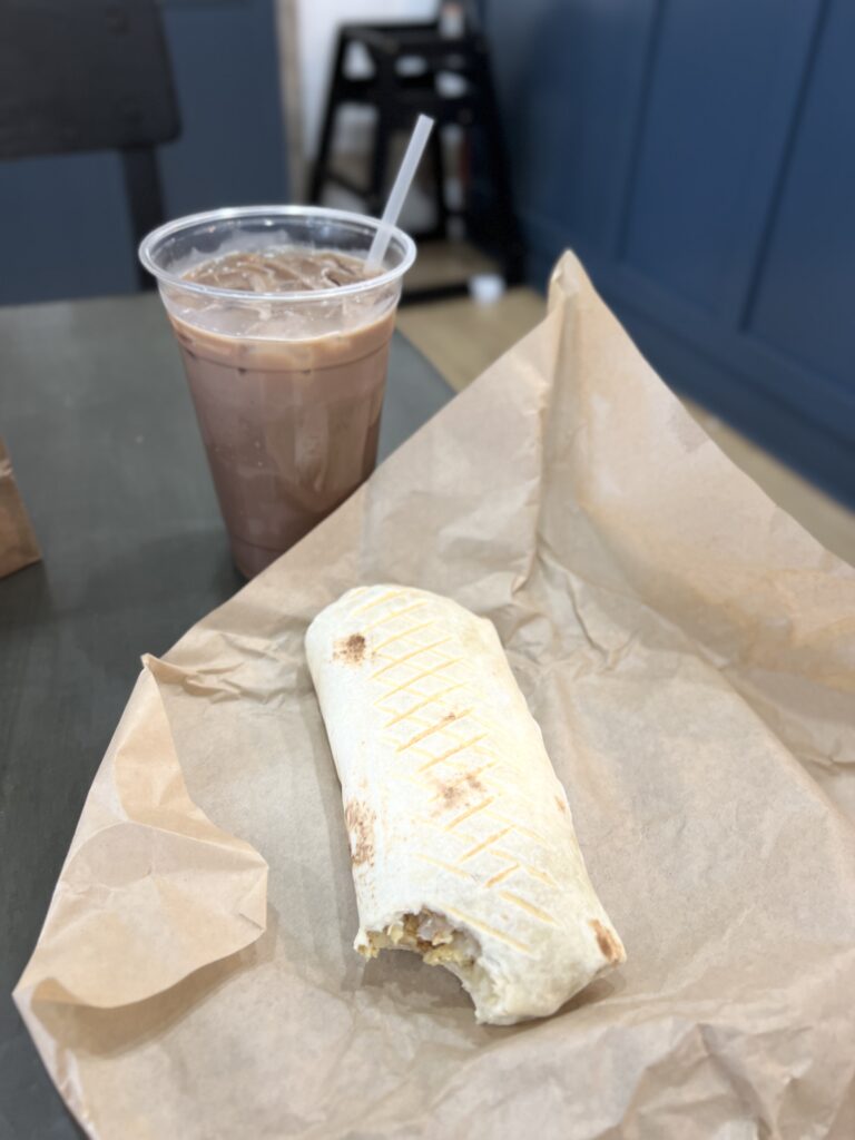 An iced coffee sits next to a breakfast burrito on a wood table. Photography by Alex Warner