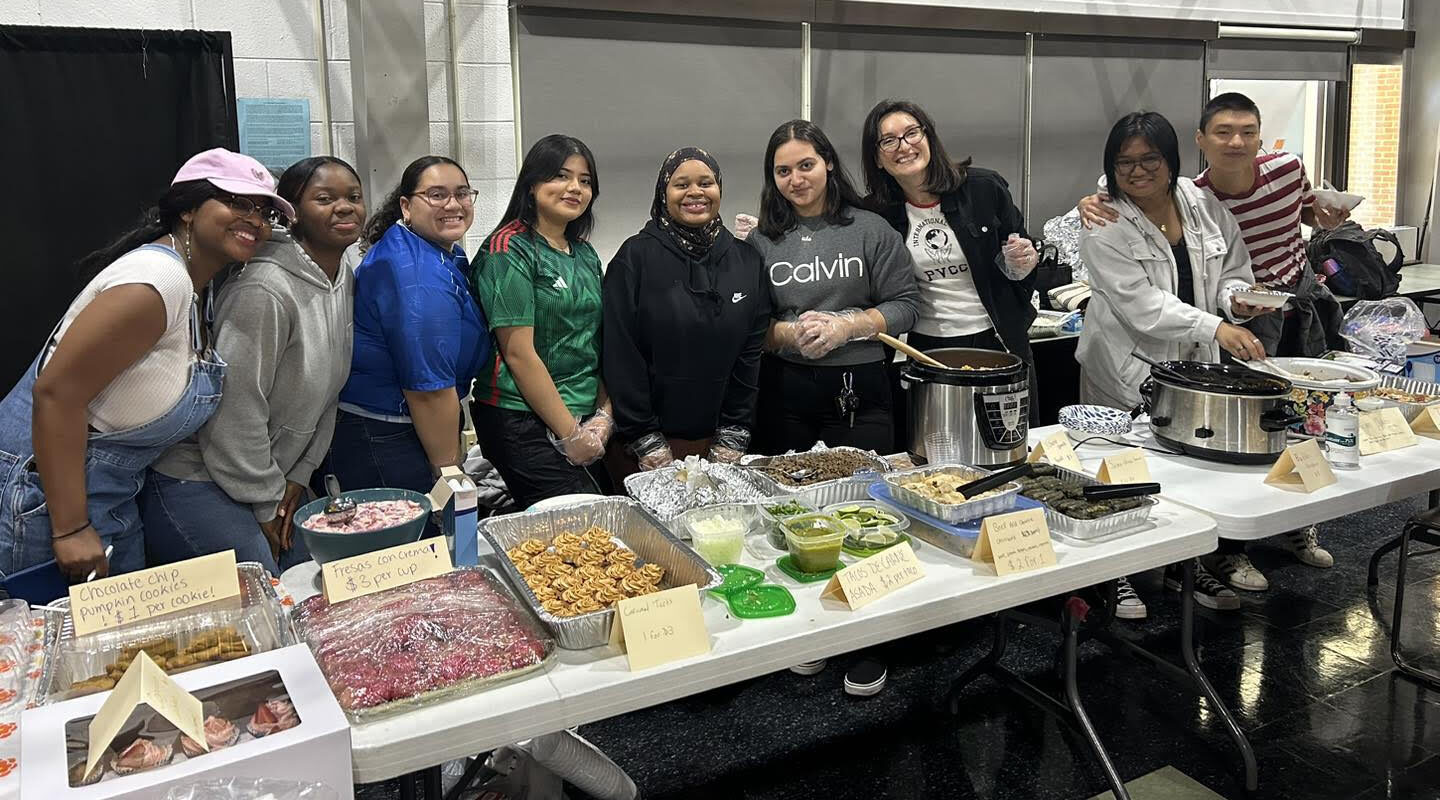 A group of people huddle for a photo in front of a table lined with various food from different cultures.