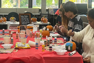 Various students sit around a table painting pumpkins.