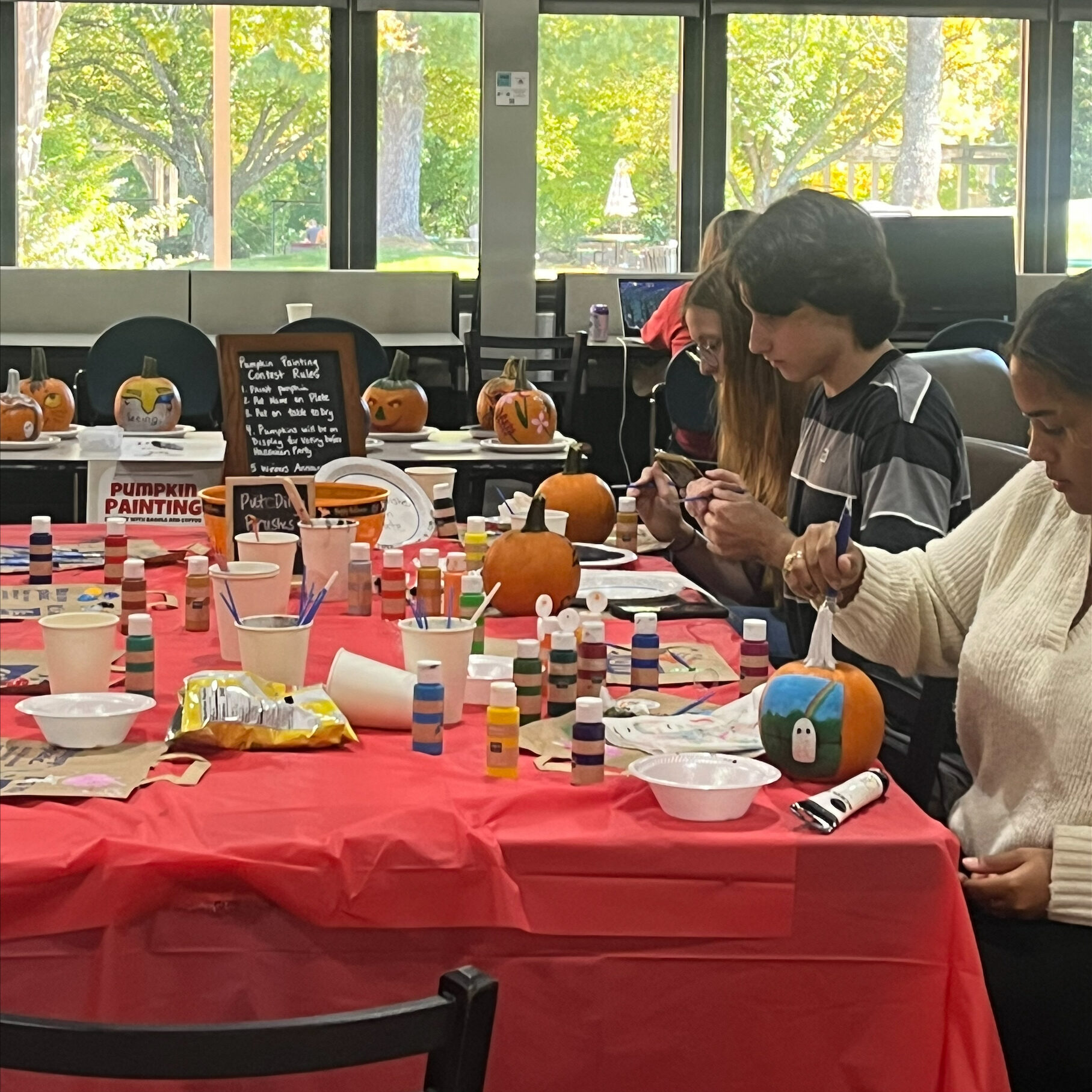 Various students sit around a table painting pumpkins.