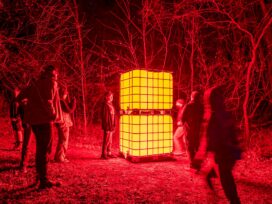 People in winter gear stand around a tall, glowing rectangular sculpture giving off red light.