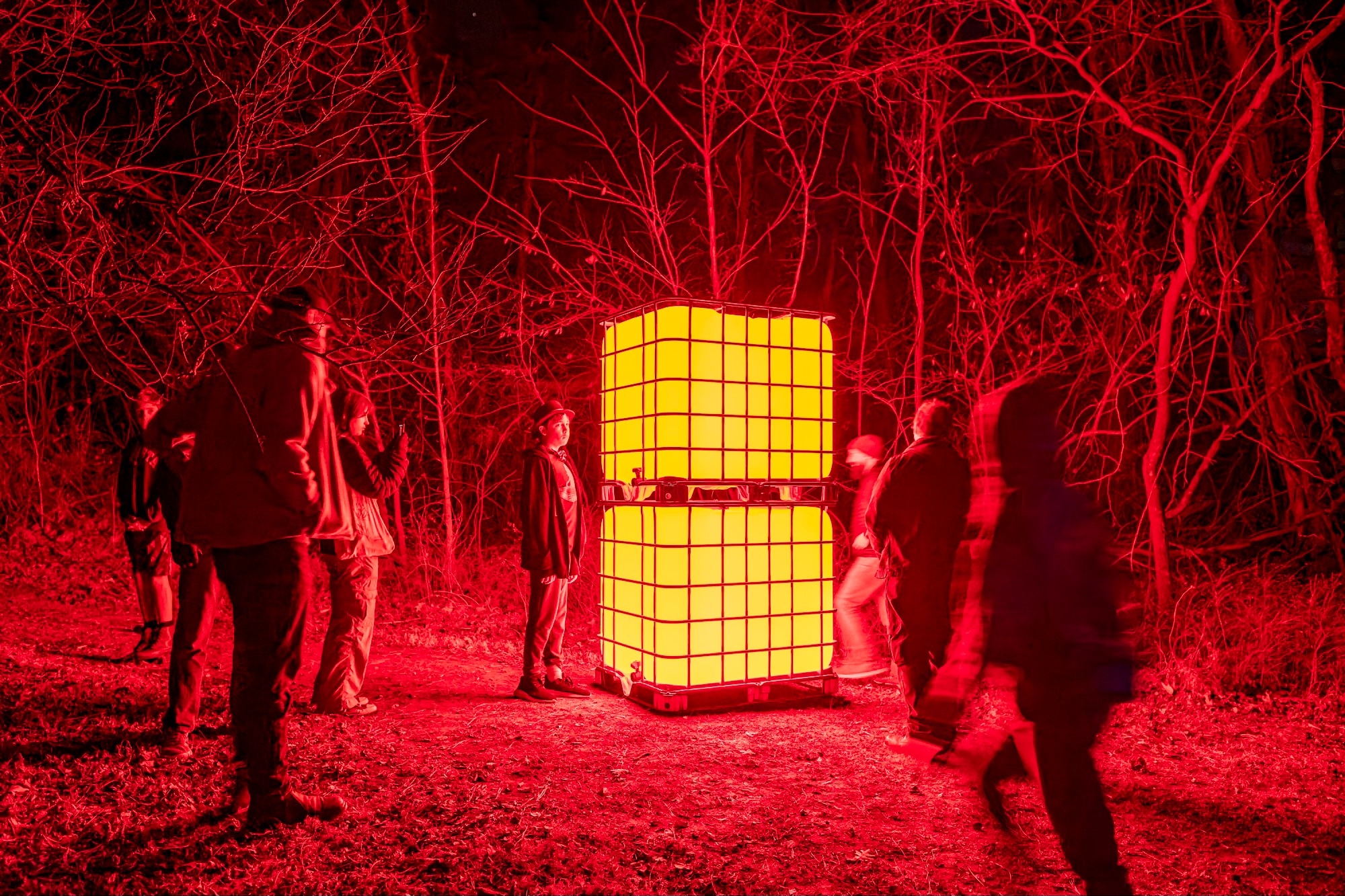 People in winter gear stand around a tall, glowing rectangular sculpture giving off red light.