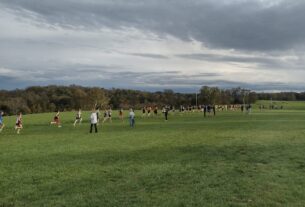 A row of high school students running in a long open field on an overcast day