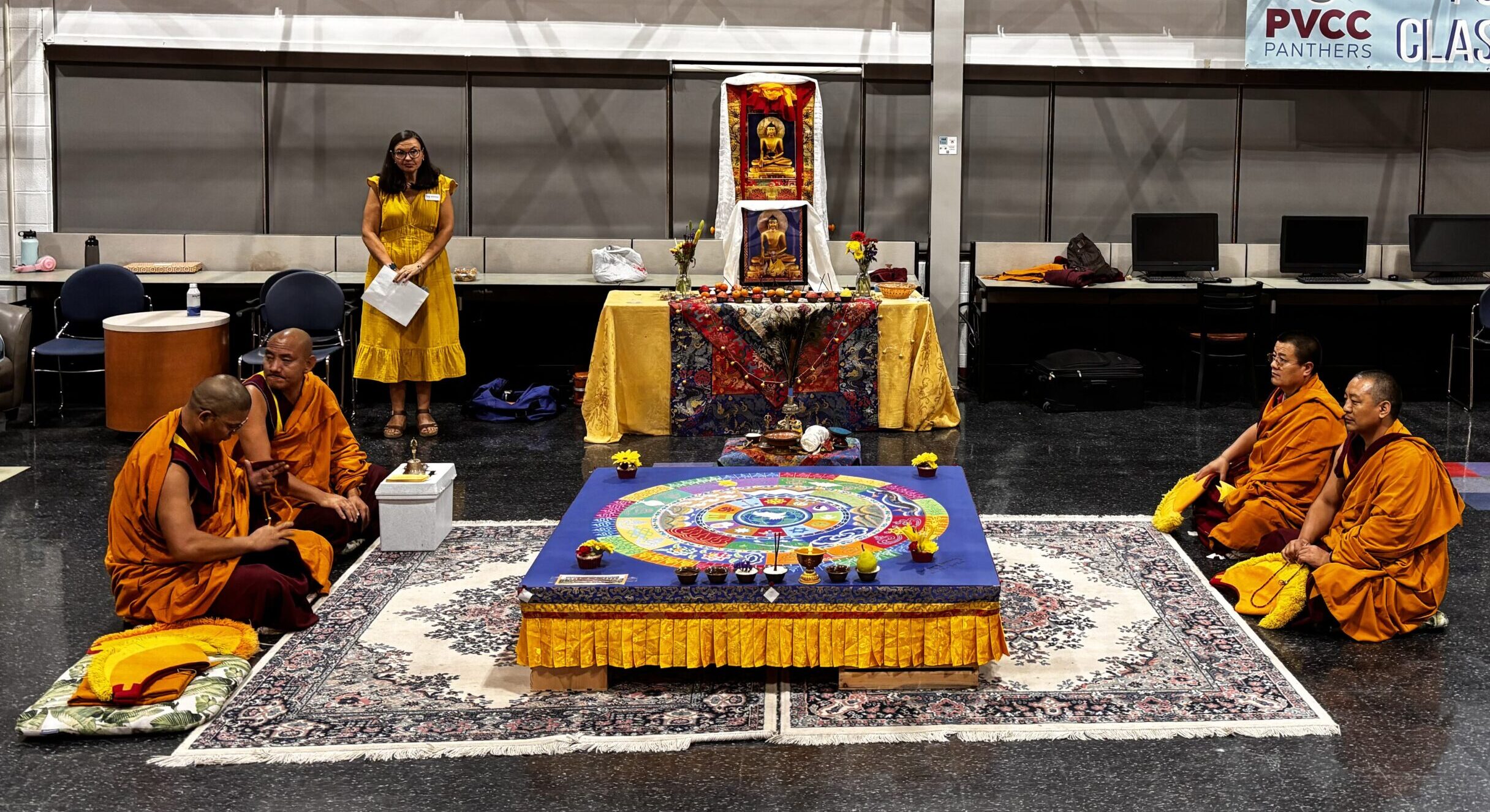 Mary-Evelyn Sellars stands behind the four monks sitting around the sand mandala before the event begins.