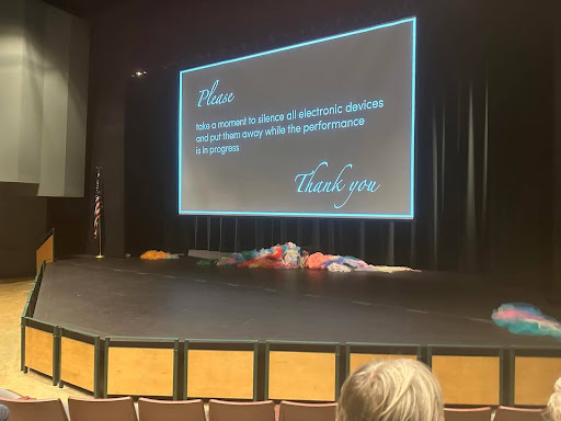 A screen projection over a stage states to have all electronic devices put away before the show begins.