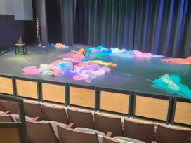 Various strands of colored cloth lay astrewn on a stage lit by colored lights.