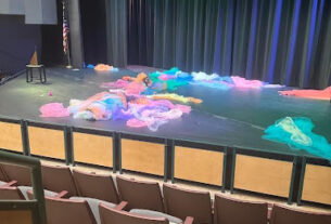 Various strands of colored cloth lay astrewn on a stage lit by colored lights.