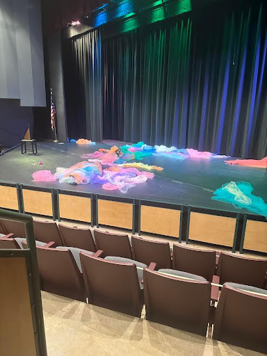 Various strands of colored cloth lay astrewn on a stage lit by colored lights.