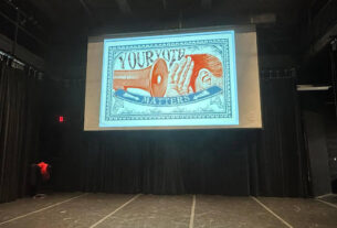 PVCC's Black Box Theater with a projection of a sign which reads "Your Vote Matters" with the graphic of a megaphone pointed at a cupped hand next to an ear.